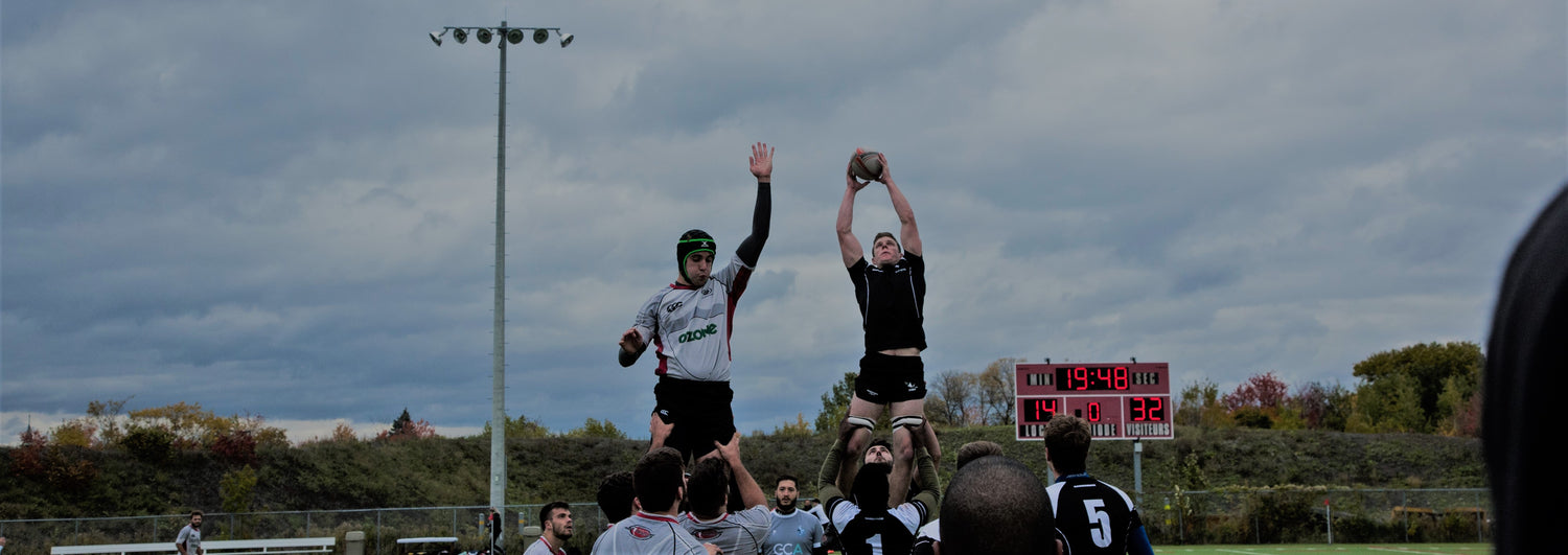 two rugby players competing in a lineout with one catching a rugby ball at a field