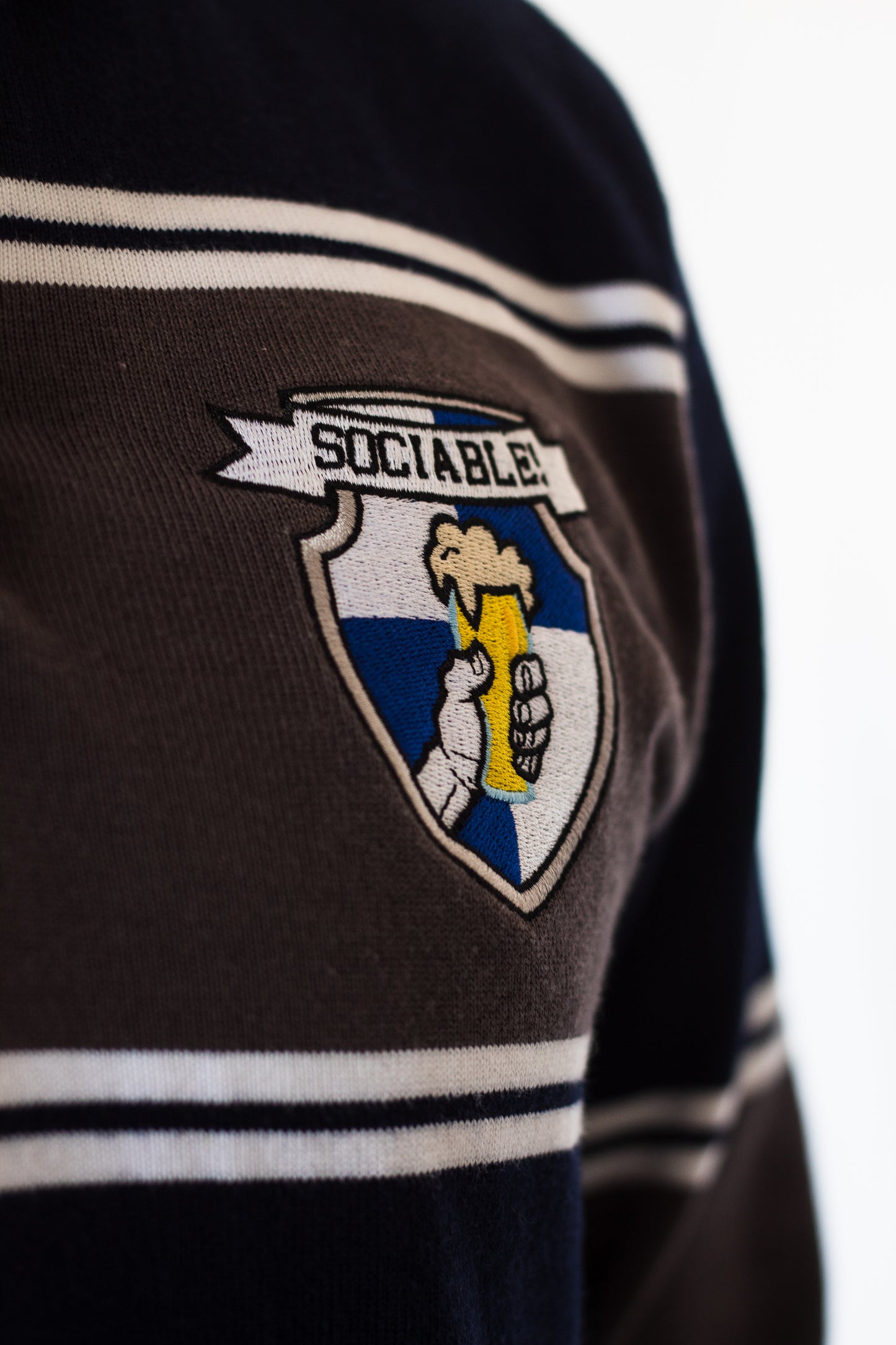 An embroidered sociable beer crest on a blue and grey rugby shirt